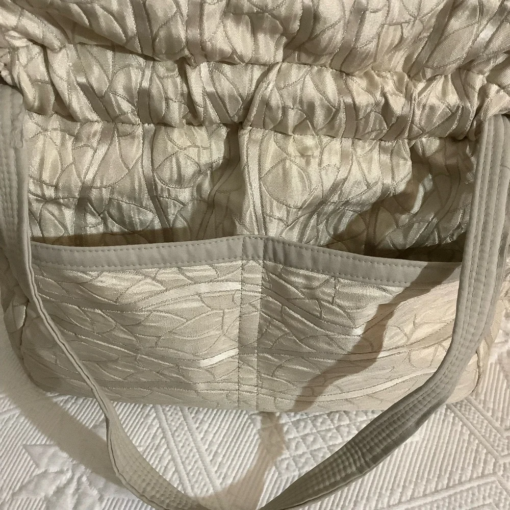 FABRIC SHOULDER BAG WITH OUTSIDE SURROUNDING POCKETS IN A CREAM AND TAUPE COLOR.